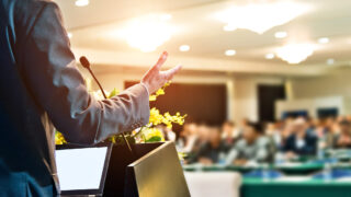 3 Techniques for a Powerful Presentation Style That Works Anywhere on Earth Man speaking to an audience with a winning presentation style under warm lighting