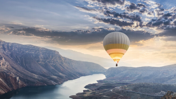 A hot air balloon floats over a river running toward a sunset, showing how to motivate yourself toward goals