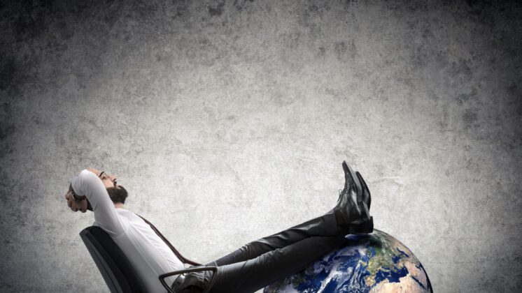 Man leans back in office chair with his feet up on a globe, showing little concern for geopolitical risk