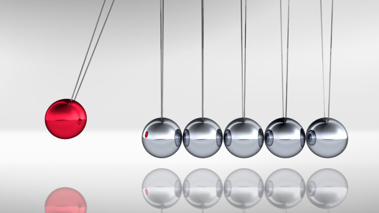 A Newton's cradle with one red ball flying out away from aligned silver balls, representing the paradoxes often present in Japanese business culture