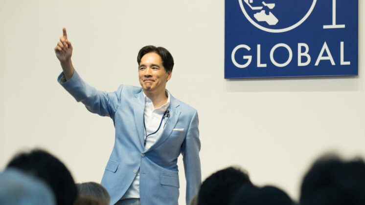 Yoshito Hori stands on stage before the G1 Global logo