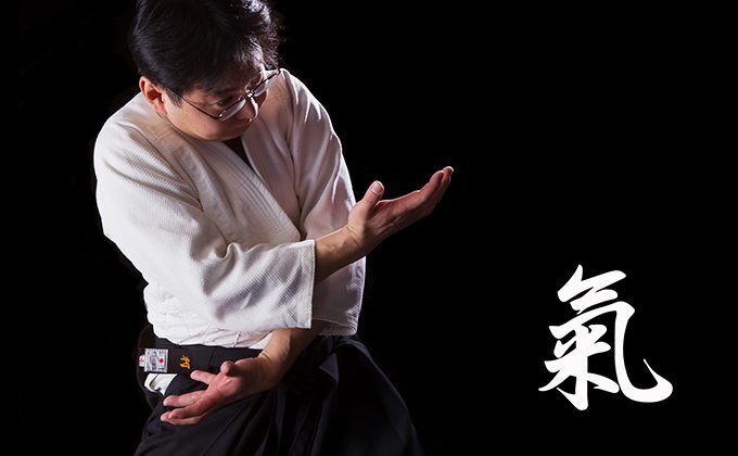 Tomoya Nakamura in aikido gear crosses his arms over his body with kanji beside him