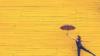 How NOT to Kill Your Passion A woman holds an umbrella in front of a yellow wall.