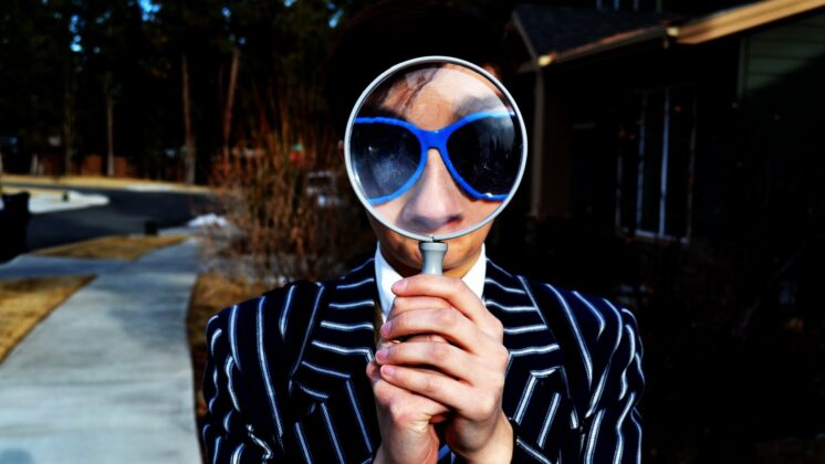 Man holding up a large magnifying glass to his face