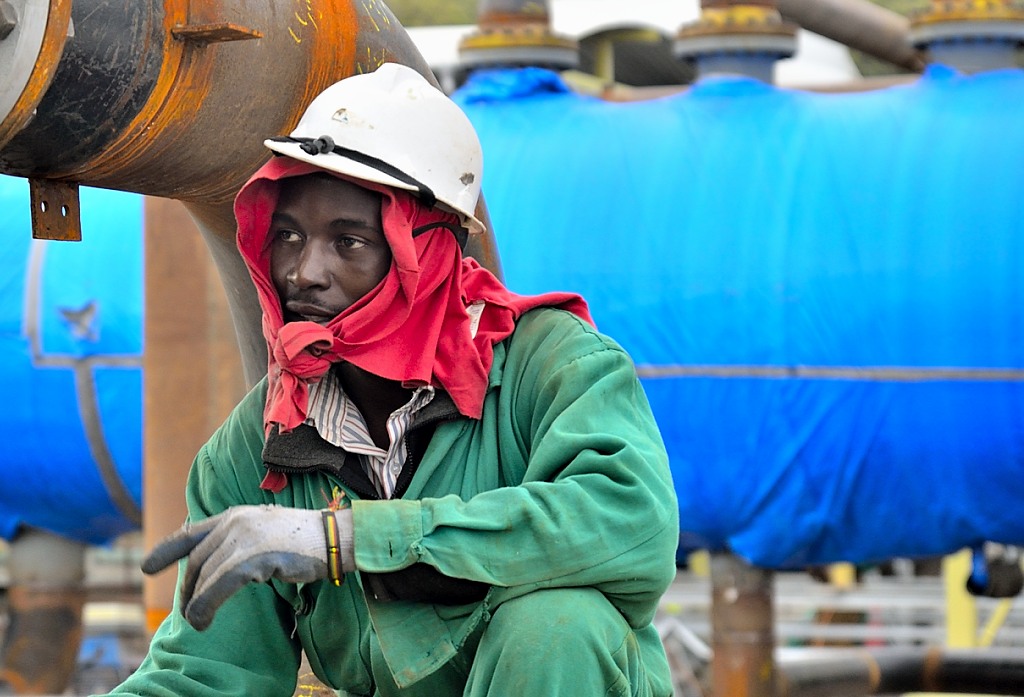 A Kenyan worker sits wearing a red scarf and a white hardhat.