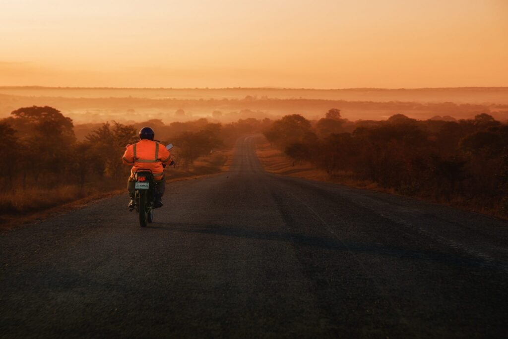 A lone biker in an orange jacket driving down the Great East Road of Zambia in the orange evening light
