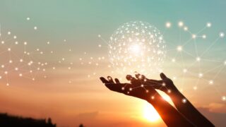 How Promoting the Invisible Heart Will Bring the Investment Impact Revolution Hands reach up against a sunset with a globe of human icons linked to external points across the sky