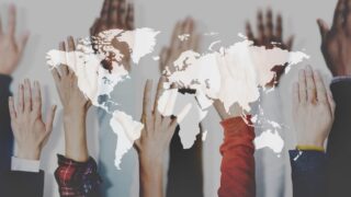 Evolving Japanese Society with Diversity and Equality in the Office Hands of various ethnicities rise up behind a superimposed map of the world