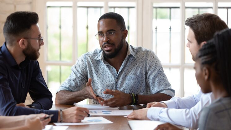Concentrated Black male manager talks to diverse colleagues in the office.