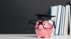 A pink piggy bank with glasses and a graduation hat beside a stack of books, representing how education and student loans go hand in hand