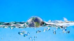 A blue background showing a cross-section of water with bubbles below the surface and a larger bubble reflecting the world just breaking the surface