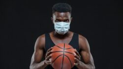 Black male basketball player in protective mask is holding a ball, preventing the spread of coronavirus infection