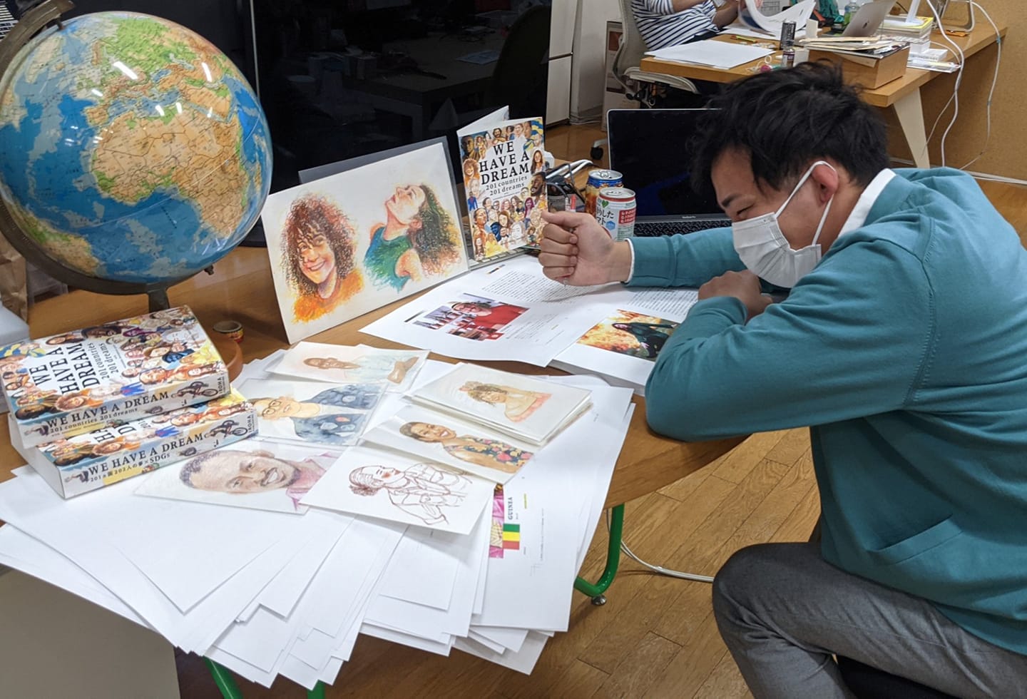 Ichikawa sits hunched over a table of sketches and drafts for WE HAVE A DREAM