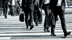 Office workers in uniform suits crossing a street on their way to the office, a common sight in Japanese working culture