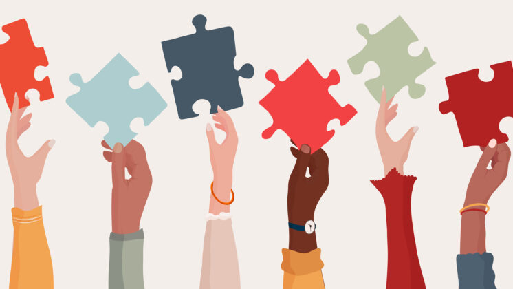 A row of multiracial women's hands lift up puzzle pieces to show the importance of thinking through a DEI business strategy