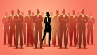 Japanese Women in Business: How to Advance Your Career Despite Inequality A woman stands in a spotlight among a crowd of businessmen, showing the gender equality odds of Japanese women in business