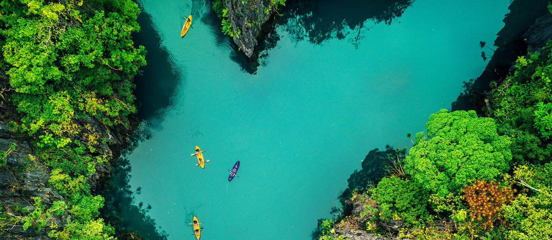 A canyon of bright green foliage and blue water with kayaks showing the power of sustainable development in the Philippines