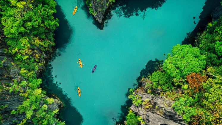 A canyon of bright green foliage and blue water with kayaks showing the power of sustainable development in the Philippines