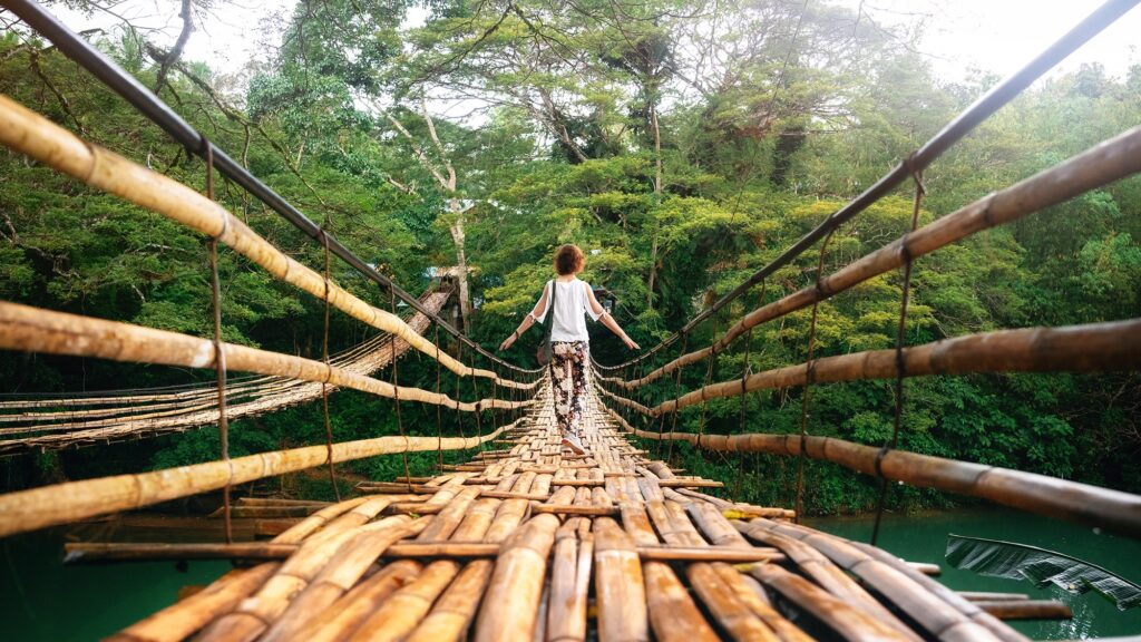 A young woman walks along a bamboo suspension bridge in the Philippine jungle