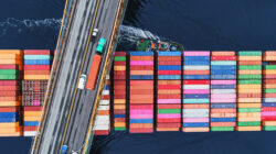 A container ship passes beneath a suspension bridge, delivering products for globalization