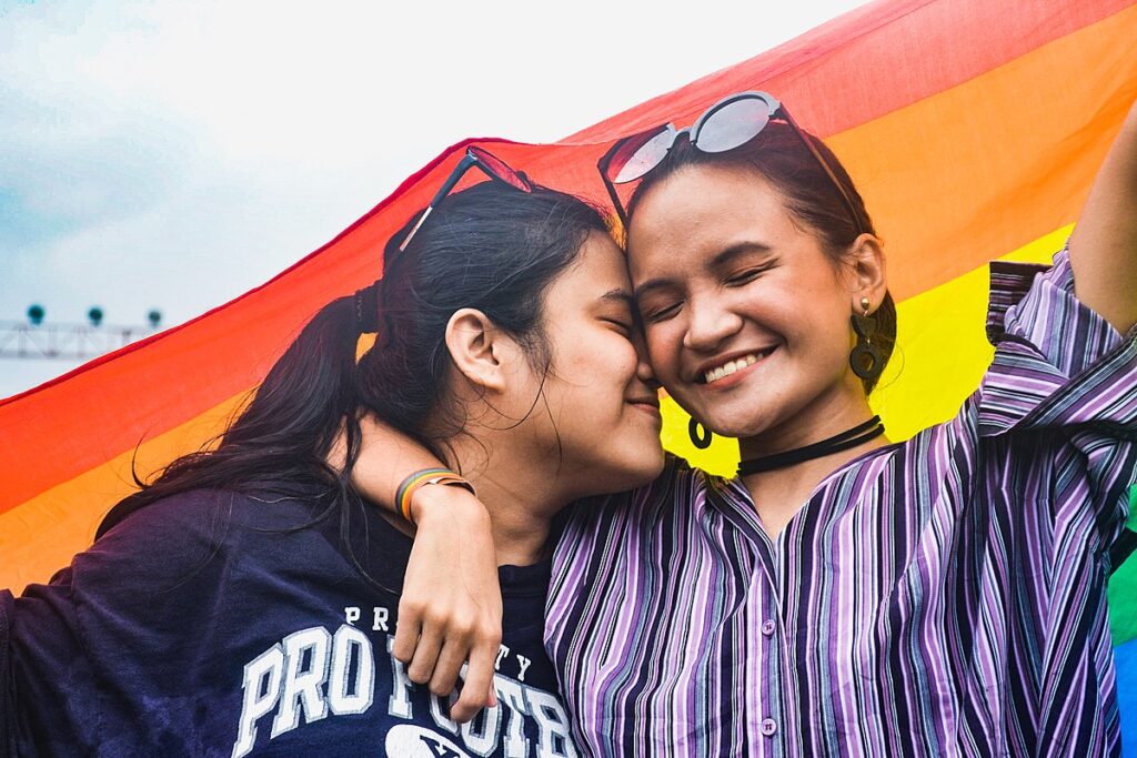 Two women smile under a rainbow flag at 2019 Metro Manila Pride