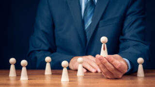 How to Avoid Management Bias in the Workplace A man in a suit raises up one employee peg above others, showing management bias in the workplace