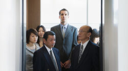 An image of a Western man standing in an elevator full of Japanese salarymen.