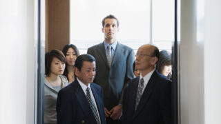 Unlock the Mysteries of Japanese Work Culture An image of a Western man standing in an elevator full of Japanese salarymen.