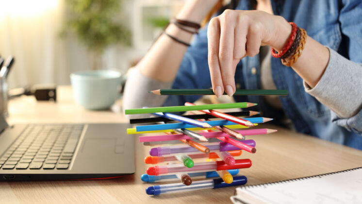 Bored woman at work in need of productivity tips builds a colorful stack of pens and pencils