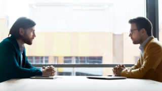 Positional Negotiation: How to Deal with Inflexibility Two men in suits participating in a positional negotiation sternly sitting across from each other