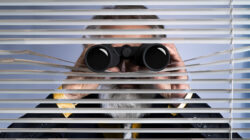 A boss suffering from productivity paranoia spying on his workers with a pair of binoculars.